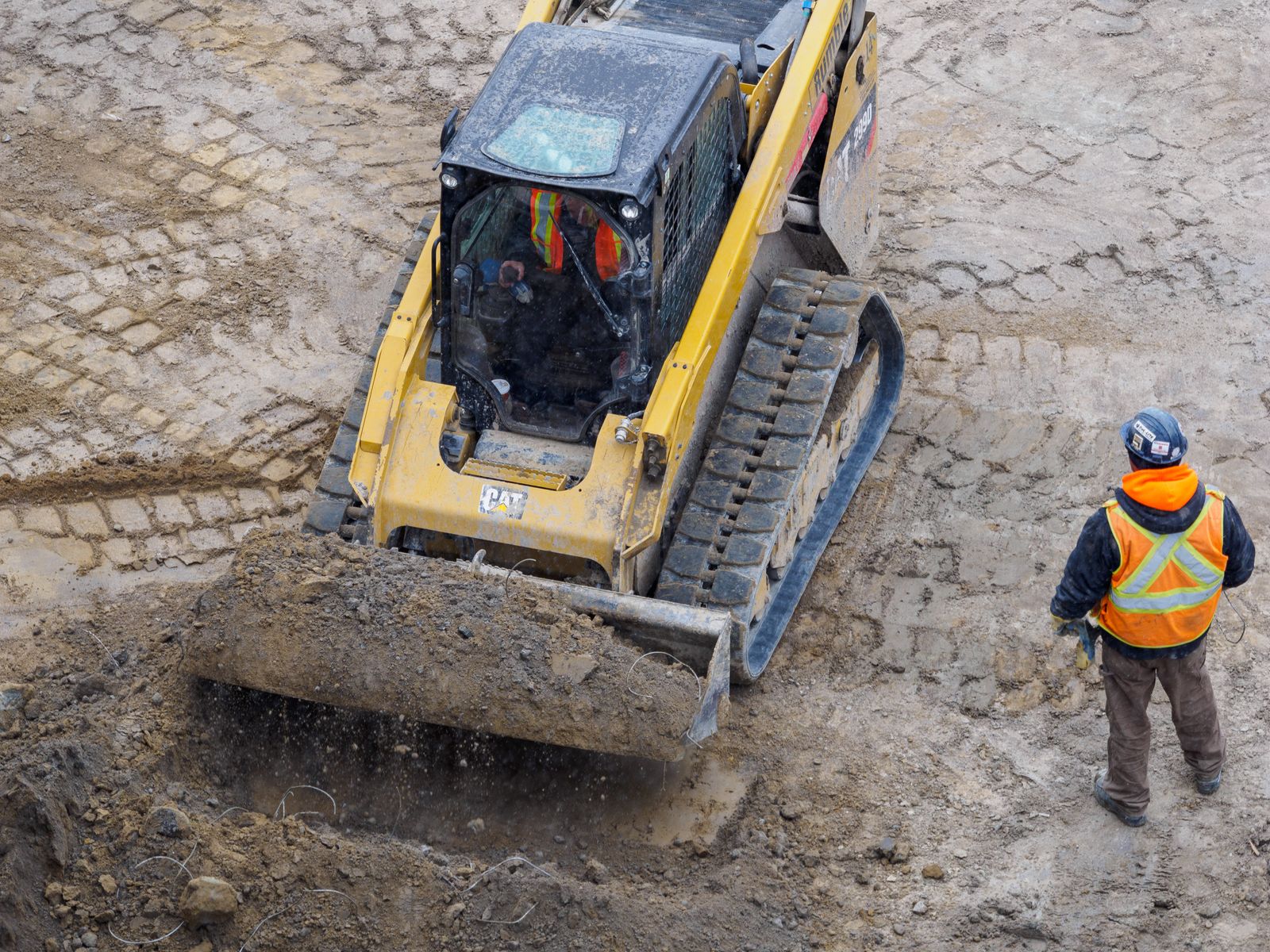 Equipment operator and safety-conscious crew working on graded earth